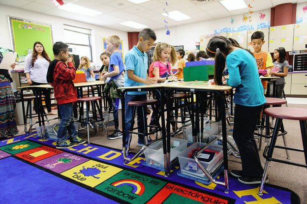 A group of young students work in a classroom using standing desks.
